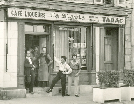 Sur la place du village, le café Forgeon au début des années 50. Détail du groupe. Charles Forgeon pose en tablier sur le pas de porte de son établissement (coll. part. carte ayant circulé en novembre 1954)